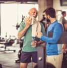 Older man speaking with trainer at the gym learning about how exercise benefits prostate health